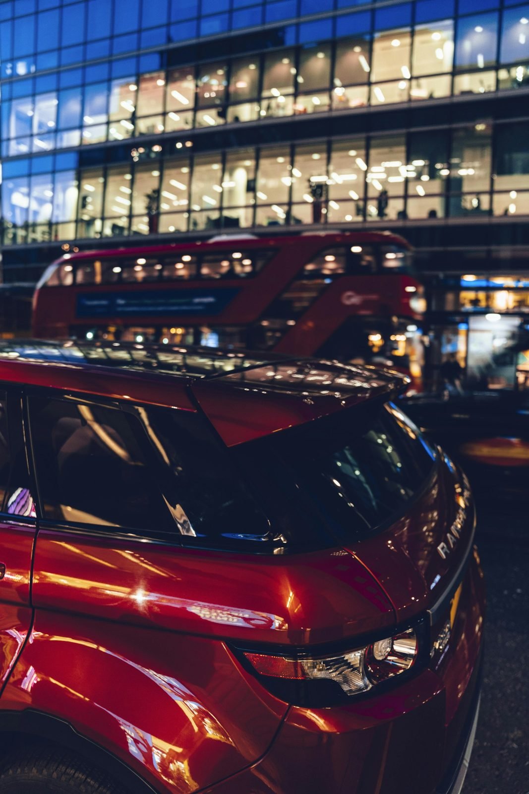 A modern London building at dusk with a red double-decker bus passing